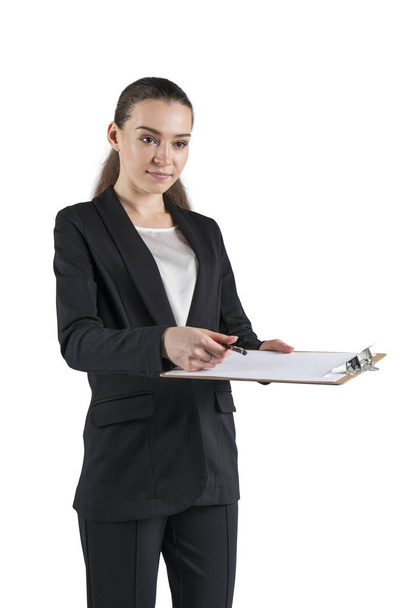 Isolated portrait of serious young businesswoman in black suit holding clipboard and pen and giving it to you to sign - Fotoğraf, Görsel