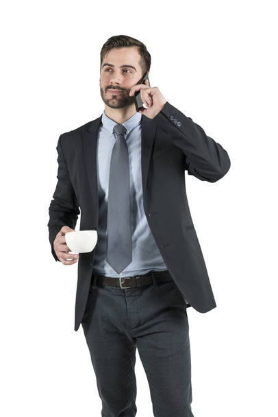 Isolated portrait of young friendly businessman talking on smartphone and holding cup of coffee. Concept of communication - Foto, imagen