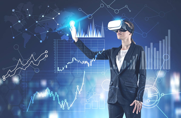 Young businesswoman in black suit and VR glasses working with interactive business infographics interface. Toned image double exposure - Фото, зображення