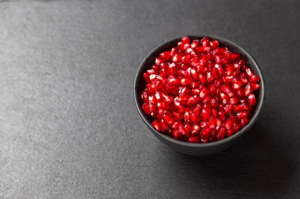 grains of pomegranate fruit in a plate on a black background. space for tex - Valokuva, kuva