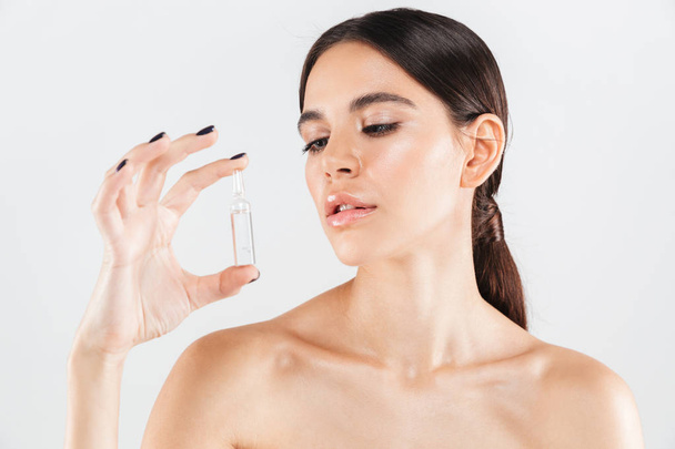 Beauty portrait of an attractive healthy woman standing isolated over white background, showing a glass capsule with liquid - 写真・画像