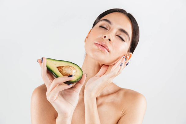 Beauty portrait of an attractive healthy woman standing isolated over white background, posing with avocado - Фото, изображение