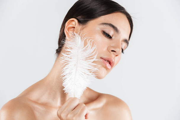 Beauty portrait of an attractive healthy woman standing isolated over white background, posing with a feather - 写真・画像