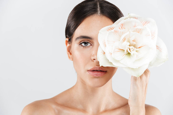 Beauty portrait of an attractive sensual healthy woman standing isolated over white background, posing with a flower - Φωτογραφία, εικόνα