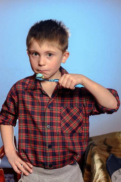 Un niño triste en pijama no está dispuesto a cepillarse los dientes antes de irse a dormir sobre un fondo azul 2019
 - Foto, imagen