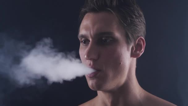 Vaper hombre guapo exhalando grandes nubes de humo con vapor de cigarrillo electrónico sobre fondo negro en cámara lenta
 - Imágenes, Vídeo