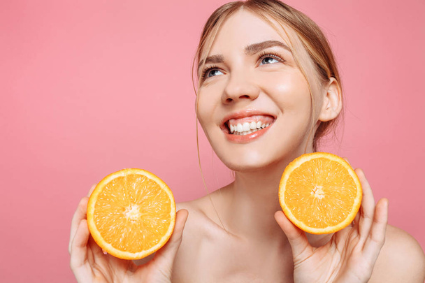 Portrait of a cheerful feminine girl, natural clear skin, girl with two orange slices, isolated on a pink background. Skin care concept, natural beauty - Foto, immagini