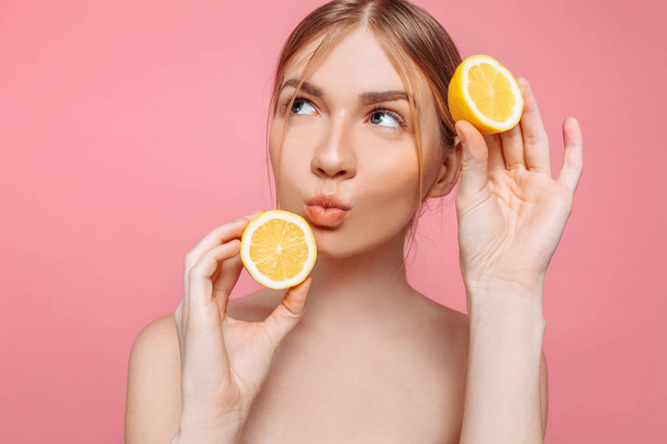 Portrait of a cheerful feminine girl, natural clear skin, girl with two lemon slices, isolated on a pink background. Skin care concept, natural beauty - Foto, Bild