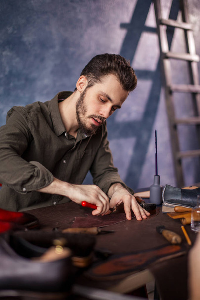 young active man cutting black leather with special knife - Фото, зображення