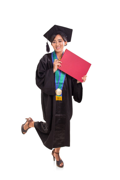 A happy graduating female student standing with one leg lifted up, full body portrait on white background, studio shot - Photo, Image