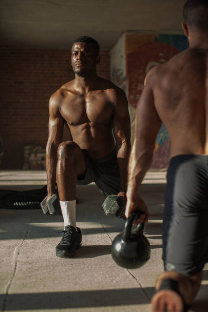 Two multiracial male athletes making lunges with weight in indoor workout - Fotoğraf, Görsel