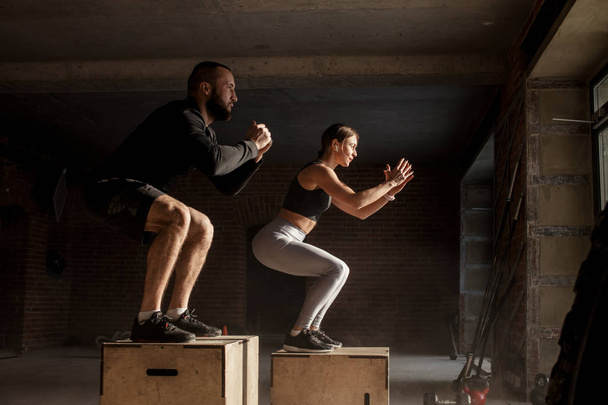 Man and woman jumping tohether on boxes in gym, funcrional workout for people - Foto, Bild