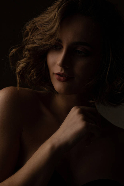 Fantastische brunette meisje met krullend haar draagt lingerie poseren met contrast licht in studio - Foto, afbeelding
