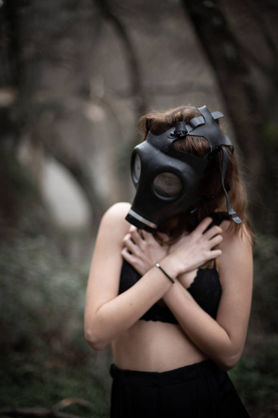 Portrait of anonymous woman in black clothes and gas mask standing in amazing spooky forest - Photo, Image