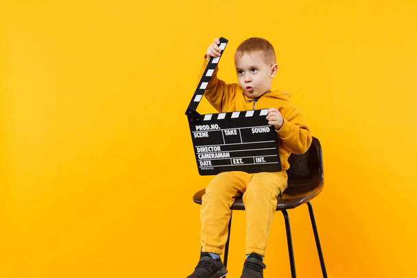 Little kid boy 3-4 years old in yellow clothes isolated on orange wall background, children studio portrait. People childhood lifestyle concept. Hand hold film making clapperboard. Mock up copy space - Foto, imagen