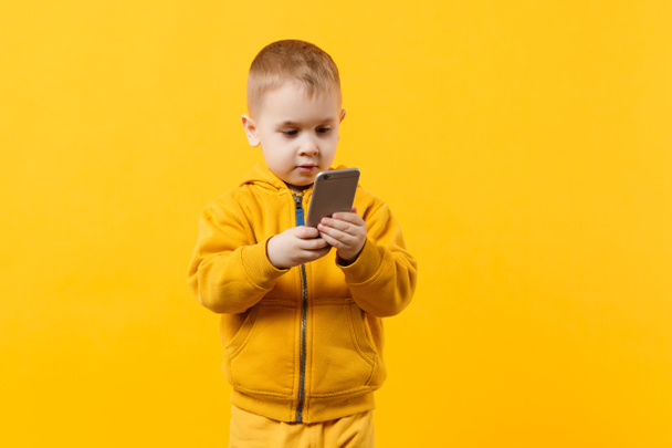 Piccolo ragazzo figo di 3-4 anni in abiti gialli che parla sul telefono cellulare isolato su sfondo arancione parete, ritratto in studio. Problema di bambini e gadget. Il concetto di stile di vita. Falsificare spazio di copia
 - Foto, immagini