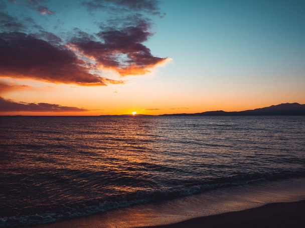 Pôr do sol visto da praia vazia - montanhas no horizonte
 - Foto, Imagem
