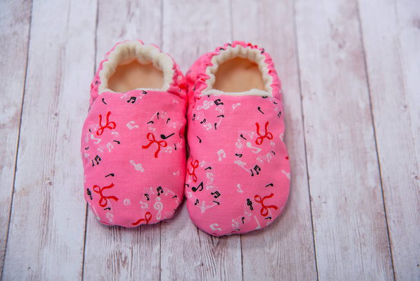 新生児の生地スリッパ。素材で作られた靴。新生児用ピンクのブーティ。複数の色の素材で作られたブーツ。小さな子供のためのスリッパ。木製の背景に赤ちゃんスリッパ. - 写真・画像