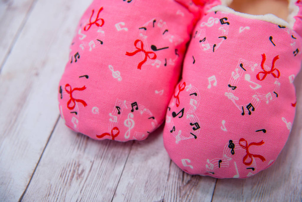 Pantoufles en tissu pour nouveau-nés. Chaussures en matériau. Chaussons roses pour nouveau-nés. Chaussons en matériau multicolore. Pantoufles pour petits enfants. Babouches bébé sur fond en bois
. - Photo, image