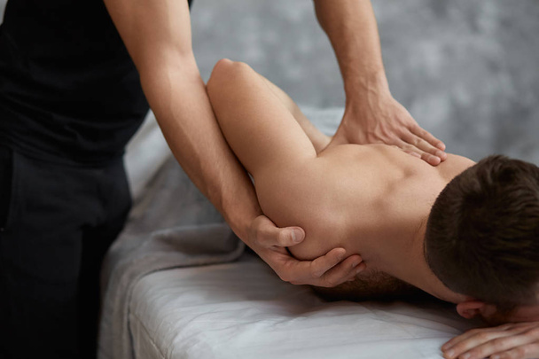 Young handsome man enjoying a back massage. Professional massage therapist is treating a male patient in apartment. Relaxation, beauty, body and face treatment concept. Home massage. - Photo, image