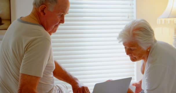 Side view of Caucasian senior couple using laptop on bed in bedroom at comfortable home. They are drinking coffee 4k - Imágenes, Vídeo