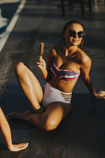 Νεαρή γυναίκα τρώει παγωτό κοντά στην πισίνα, σε ζεστή μέρα του καλοκαιριού - Φωτογραφία, εικόνα