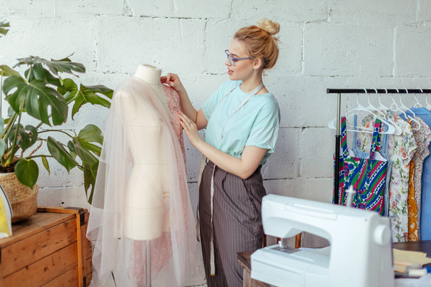Beautiful seamstress is working with a wedding dress model in her studio - Fotoğraf, Görsel