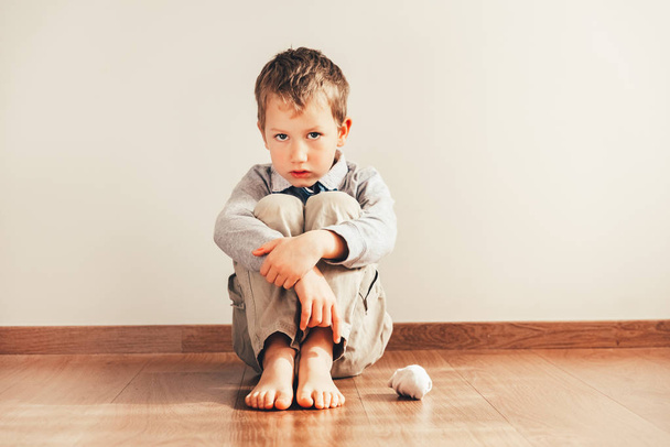 Дитина сидить на підлозі босоніж з сумним обличчям, бо не в змозі одягнути його одяг
. - Фото, зображення