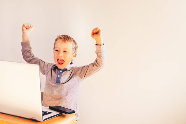 Niño usando un ordenador portátil y riéndose de su éxito en los negocios
. - Foto, Imagen