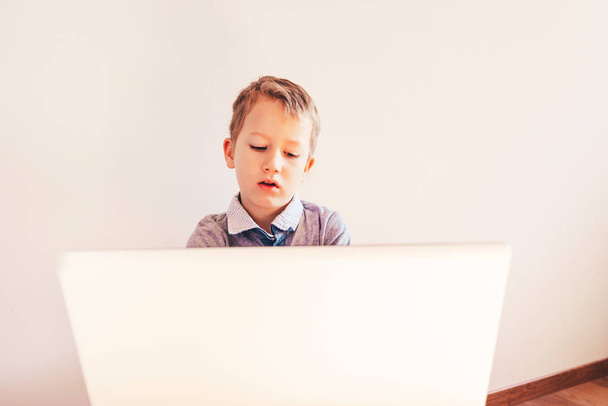 Child with very expressive face in front of a laptop with angry gesture. - Photo, Image