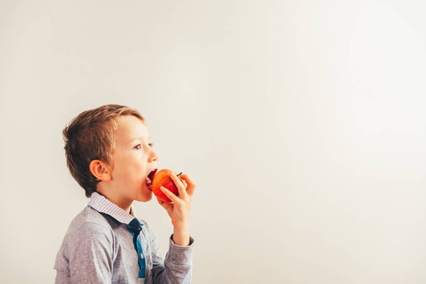 Happy child biting a tasty apple, isolated on white background from side. - Photo, Image