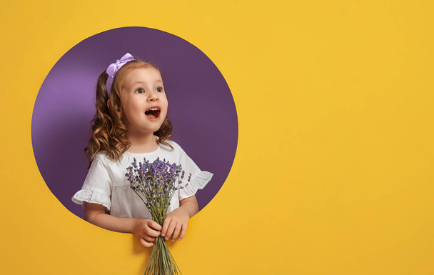 Cute child girl with a bouquet of lavender on yellow and purple background. Mothers day, spring concept. - Zdjęcie, obraz