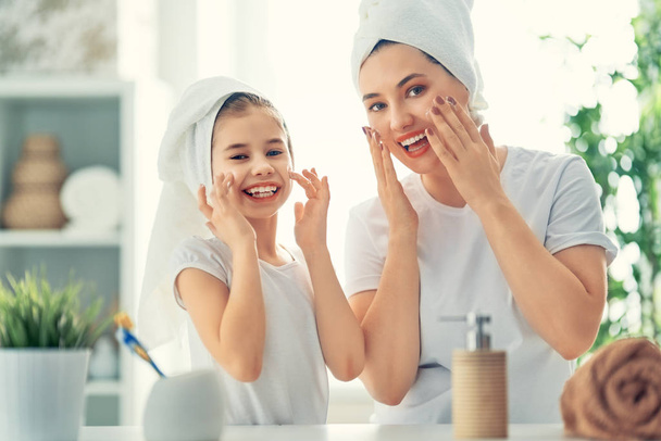 ¡Familia feliz! Madre e hija niña están cuidando la piel en el baño. - Foto, Imagen
