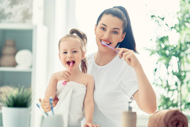 Happy family! Mother and daughter child girl are brushing teeth toothbrushes in the bathroom. - Fotó, kép