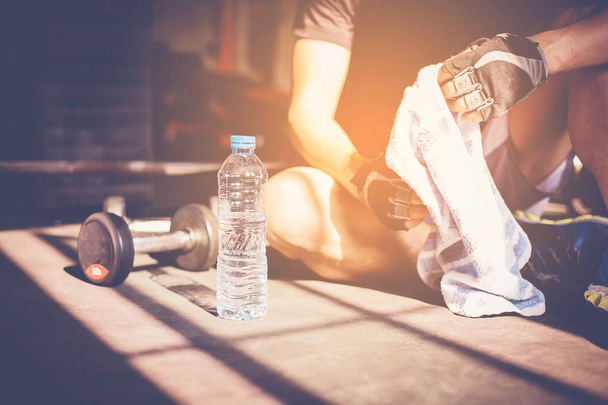 Muskelprotz im Fitnessstudio macht Trainingspause und sitzt neben der Wasserflasche - Foto, Bild