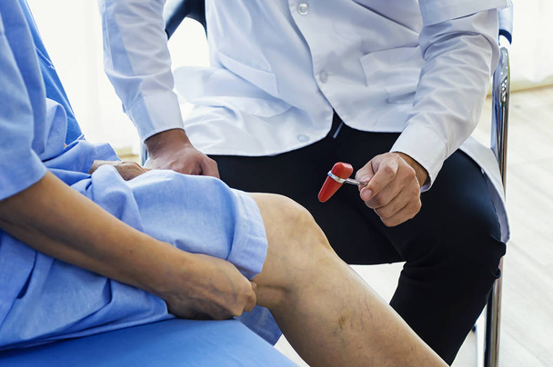 Крупним планом жінка-фізіотерапевт масажує ногу пацієнта в фізіотерапевтичній кімнаті. Чоловік лікар перевіряє з сенсорним молотком
. - Фото, зображення