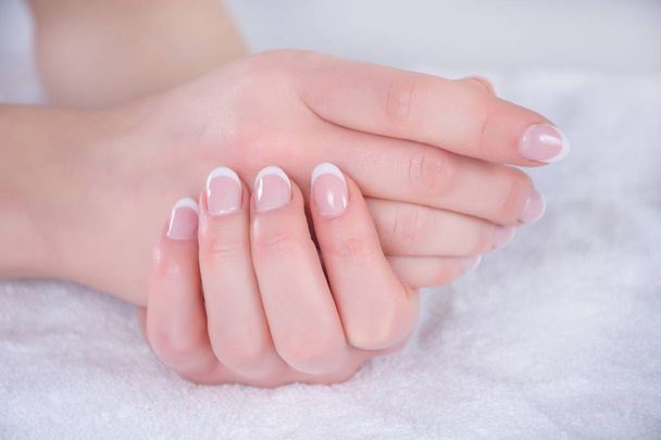 Όμορφη γυναίκα χέρια με γαλλική Πολωνικά νύχια σε λευκή πετσέτα στο studio ομορφιάς. Περιποίηση και ομορφιά έννοια. Εσωτερικη, επιλεκτική εστίαση - Φωτογραφία, εικόνα