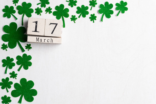 Block calendar for St Patrick's Day, March 17, with green clover leaf, green water and paper tag on white wooden background - Photo, Image
