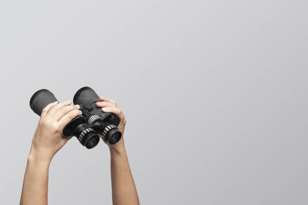 Hands holding binoculars on gray background, looking through binoculars, journey, find and search concept. - Photo, image