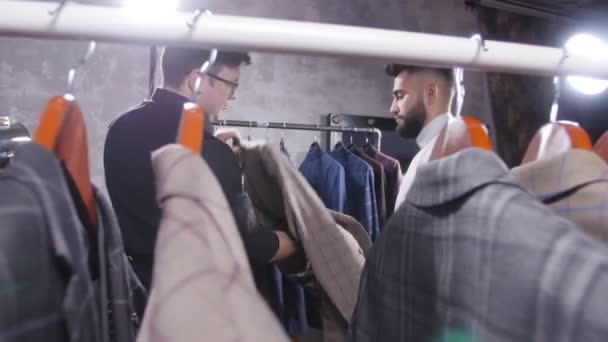 De verkoper helpt een jongeman te kiezen voor een pak in de winkel - Video