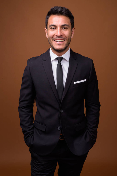 Young handsome Hispanic businessman against brown background - Φωτογραφία, εικόνα
