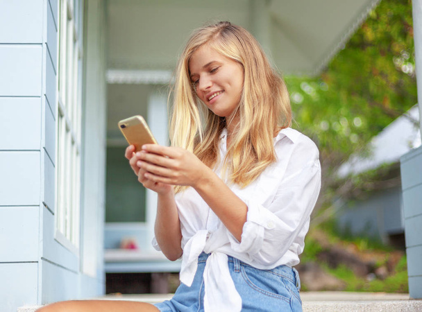 Piękna Blondynka, na dom letni taras, ze smartfonem w jej ręce, cieszy się słońcem - Zdjęcie, obraz