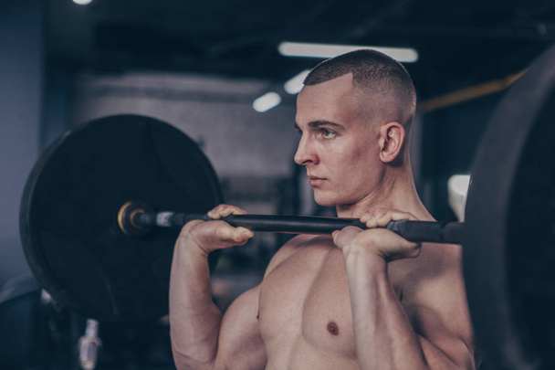 Close up shot of a shirtless muscular male athlete lifting barbell, looking concentrated. Ripped sportsman with toned torso lifting weights at the gym. Workout, lifestyle, sports concept - Fotó, kép