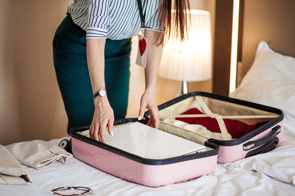 Woman in elegant clothes packing things into travel bag, departing from hotel - Фото, изображение