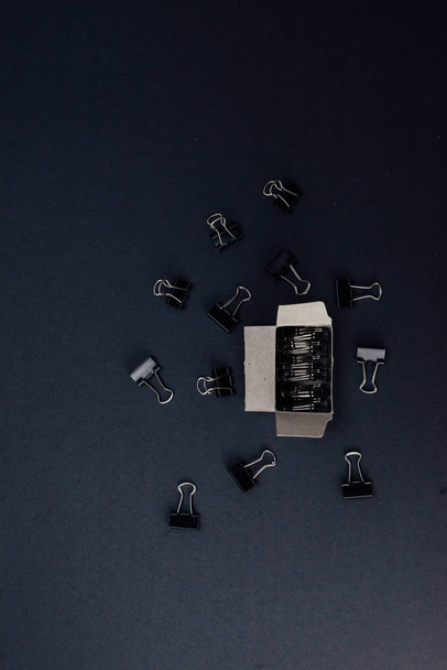 Aglutinantes de metal en colocado en una pequeña caja de papel y un montón de aglutinantes fuera de una caja que se extiende sobre un fondo negro. diseño vertical
 - Foto, imagen