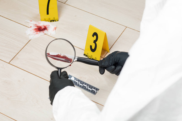 Ekspertem kryminologii przez szkło powiększające, patrząc na krwawy nóż na miejscu zbrodni. - Zdjęcie, obraz