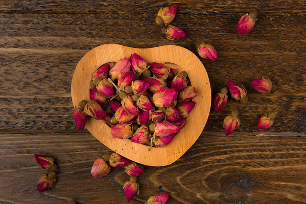 tea rose buds on the wooden saucer  isolated on wooden background, top view - Foto, Bild