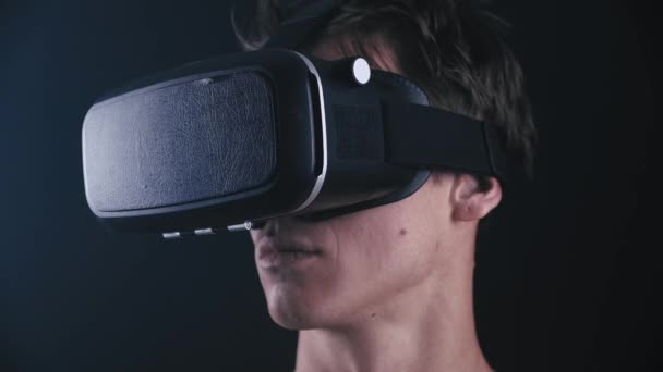 Close-up of young man getting experience using VR-headset or virtual reality glasses, standing in dark, with smoke around him in slow motion - Footage, Video