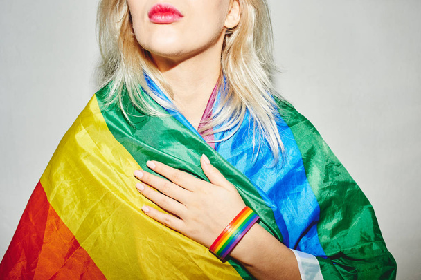A beautiful blonde young woman wearing a rainbow LGBTQ flag. Lesbian, gay, bisexual, transgender, queer. Homosexual man - Foto, afbeelding