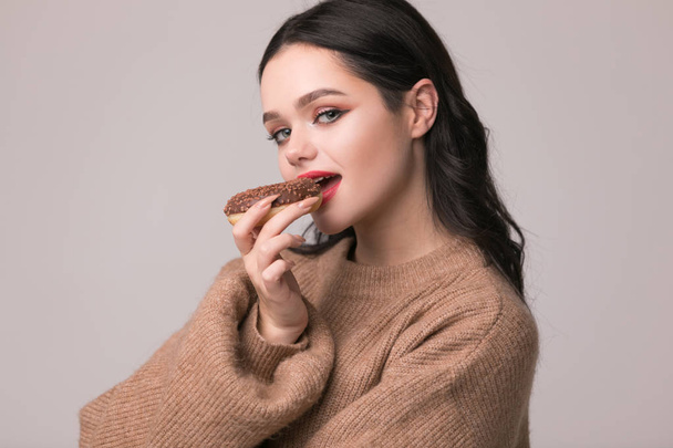 beautiful girl with red lips posing with donuts.Pretty sexy brunette girl with long hair, glossy red lips, holding tasty donut with hand, looking at camera. Dark gray background, copy space - Φωτογραφία, εικόνα